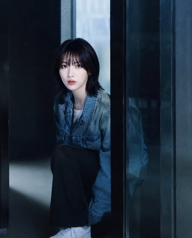 A glassh member in a denim jacket framed by blue glass panels.