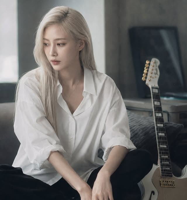 A glassh member seated beside a white electric guitar.